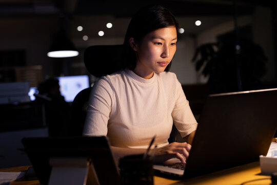 Asian businesswoman sitting at desk and using laptop, working late at office