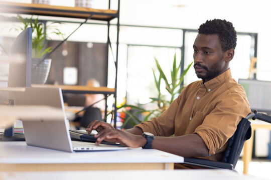 Disabled casual african american businessman in wheelchair using computer in modern office