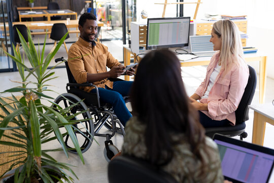 Diverse casual disabled businessman in wheelchair discussing work with colleagues in office