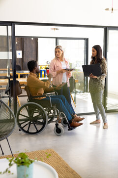 Diverse casual disabled businessman in wheelchair discussing work with colleagues in office