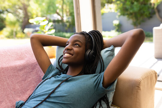Happy african american teenager girl lying on sofa and using headphones