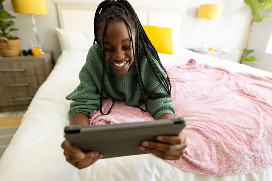 Happy african american teenager girl lying on bed, using tablet