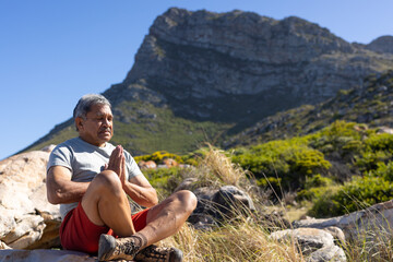 Senior biracial man doing yoga and meditating in mountains