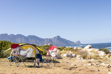 Yellow tent with camping chairs and equipment over mountains and sea, copy space
