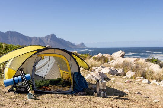 Yellow tent with camping equipment over mountains and sea, copy space