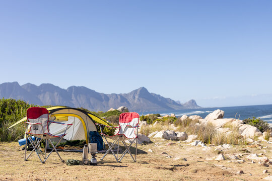 Yellow tent with camping chairs and equipment over mountains and sea, copy space