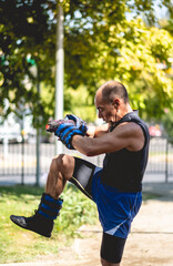 Fototapeta premium Healthy and active: ageless and muscular elderly man with sand body weights training in street workout park in the morning