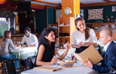 Obraz premium positive female busboy taking order to couple in modern restaurante