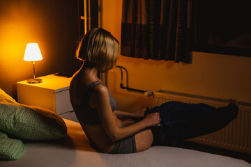 Unrecognizable woman takes off her jeans in a dark room. Relaxation after a hard day. Stay alone with yourself.