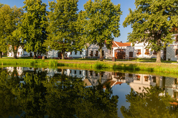 Fototapeta na wymiar Pond and traditional houses of rural baroque style in Holasovice village, Czech Republic