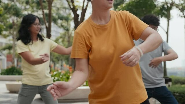 Medium shot of mature Asian woman practicing Tai chi with eyes closed while having family fitness time in park on summer day