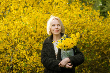 A woman looks into the distance with a bouquet of yellow flowers on a background of yellow flowers. Spring mood.