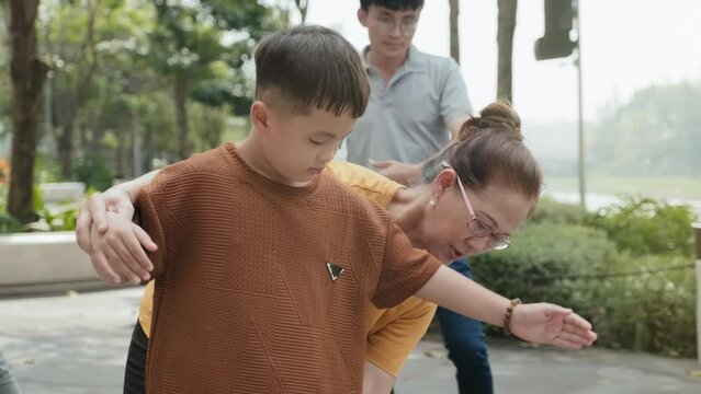 Cheerful grandma teaching little boy tai chi movements while exercising together with family in park on summer day
