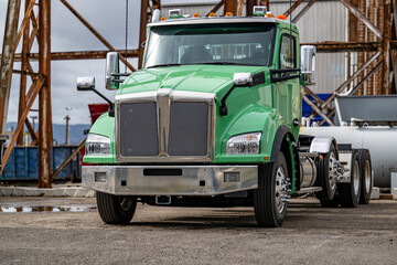 Fresh green day cab bonnet big rig semi truck tractor without the semi trailer standing on the industrial production parking side with rusty metal constructions