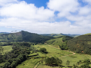 Aerial view of beautiful forest full of nature and pasture fields in Tremembé in Vale da Paraíba in São Paulo. Mountains and hills in sunny day. Lots of green and tropical vegetation. Drone