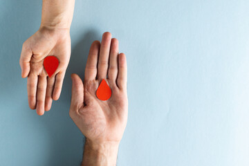 Hands of caucasian woman and man holding blood drops, on blue background with copy space