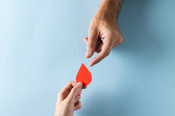 Hands of caucasian woman passing blood drop to caucasian man, on blue background