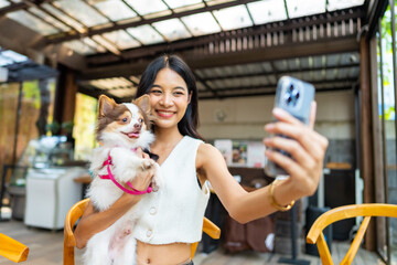 Young Asian woman using mobile phone taking selfie with her chihuahua dog at pets friendly cafe....
