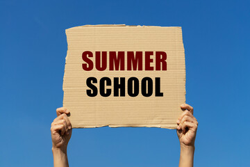 Summer school text on box paper held by 2 hands with isolated blue sky background. This message...