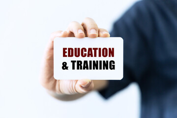 Education and training text on blank business card being held by a woman's hand with blurred background. Business concept about education.