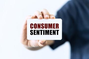 Consumer sentiment text on blank business card being held by a woman's hand with blurred background. Business concept about consumer sentiment.