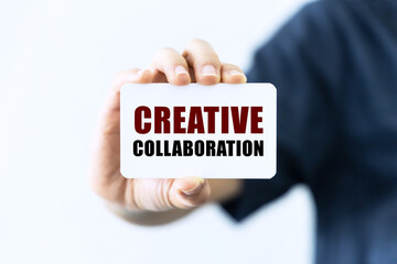 Creative collaboration text on blank business card being held by a woman's hand with blurred background. Business concept about collaboration.