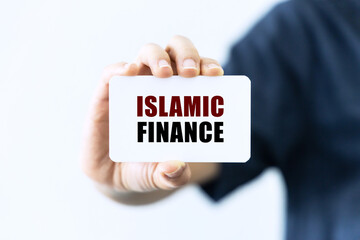 Islamic finance text on blank business card being held by a woman's hand with blurred background. Business concept about islamic finance.