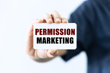 Permission marketing text on blank business card being held by a woman's hand with blurred background. Business concept about permission marketing.
