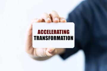 Accelerating transformation text on blank business card being held by a woman's hand with blurred background. Business concept about transformation.
