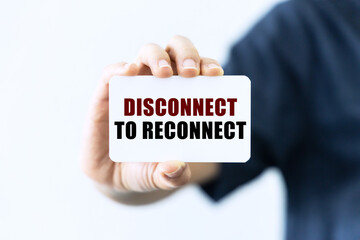 Disconnect to reconnect text on blank business card being held by a woman's hand with blurred background. Business concept about disconnect to reconnect.