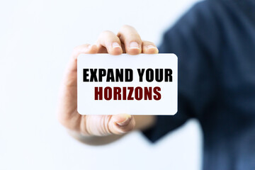 Expand your horizons text on blank business card being held by a woman's hand with blurred background. Business concept about expanding your horizons.