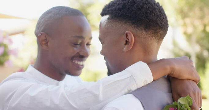 Happy african american gay male couple holding flowers and embracing at wedding, slow motion