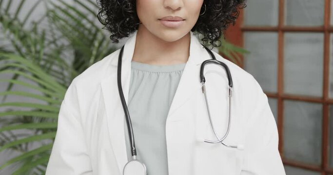 Portrait of biracial female doctor wearing lab coat, using tablet, slow motion