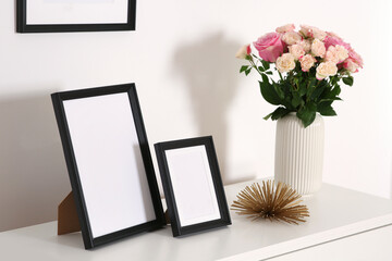 Empty frames and flowers on chest of drawers indoors