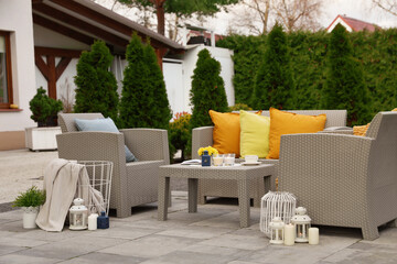 Beautiful rattan garden furniture, soft pillows and different decor elements in backyard