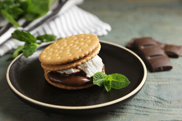 Delicious marshmallow sandwich with crackers, mint and chocolate on light blue wooden table, closeup