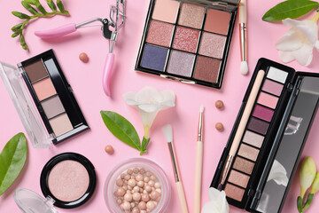 Flat lay composition with eyeshadow palettes and beautiful flowers on pink background