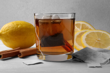 Tea bags, glass of hot drink, cinnamon sticks and lemons on white wooden table, closeup