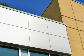 Commercial external metal composite panels on a building with blue sky and clouds in the background. The durable metal composite panels are a dark shade of grey and gold color on the modern building.