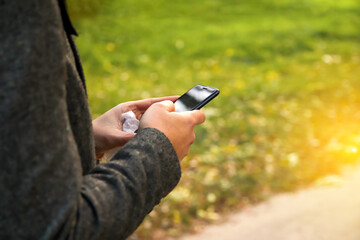 Hand phone sunny. Defocus male hand using smart phone in autumn park. Typing text message or reading social media at mobile phone. Cell phone. Communication. Out of focus