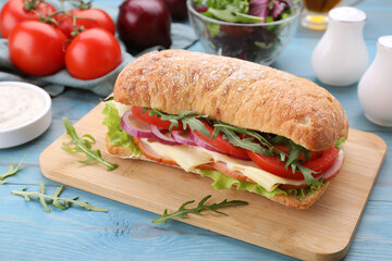 Delicious sandwich with fresh vegetables, cheese and arugula on light blue wooden table