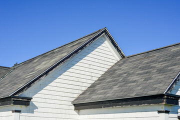 Multiple peaked and layered roofs on a white vintage wooden house. The eave is painted black. The...