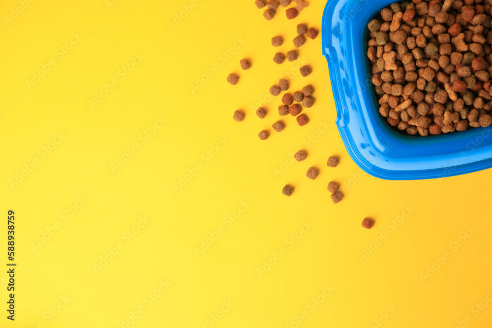 Wall mural Dry pet food in feeding bowl on yellow background, flat lay. Space for text