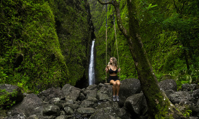 Naklejka na ściany i meble Girl hiker swings in front of a waterfall in Hawaii green jungle forest. 