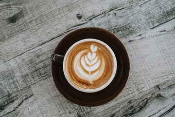 Flat lay or top view shot of a cup of coffee with beautiful Latte Art on a wooden table. Close-up.
