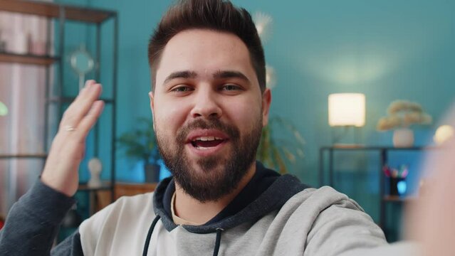 POV of Caucasian man blogger taking selfie on smartphone, communicating video call online with social media subscribers followers, recording vlog stories. Young guy at home apartment room on couch