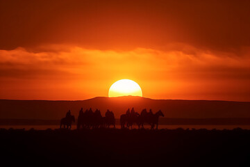 Photorealistic ai artwork of sunset with mountains and cowboys silhouetted against the sun. Generative ai.