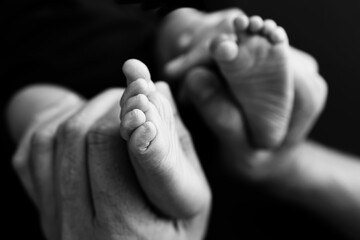 Fototapeta premium Baby feet in mother hands. Mom and her Child. Happy Family concept. Beautiful conceptual image of Maternity. Black and white photo, black background.