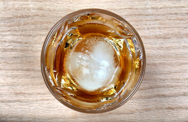 Overhead close up view of a glass of whiskey drink with round ice cube on table