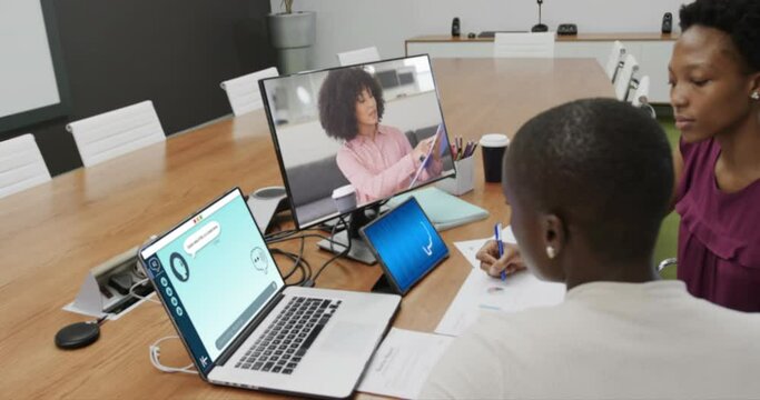 Diverse businesswomen in office using computer with video call and ai messaging on screens